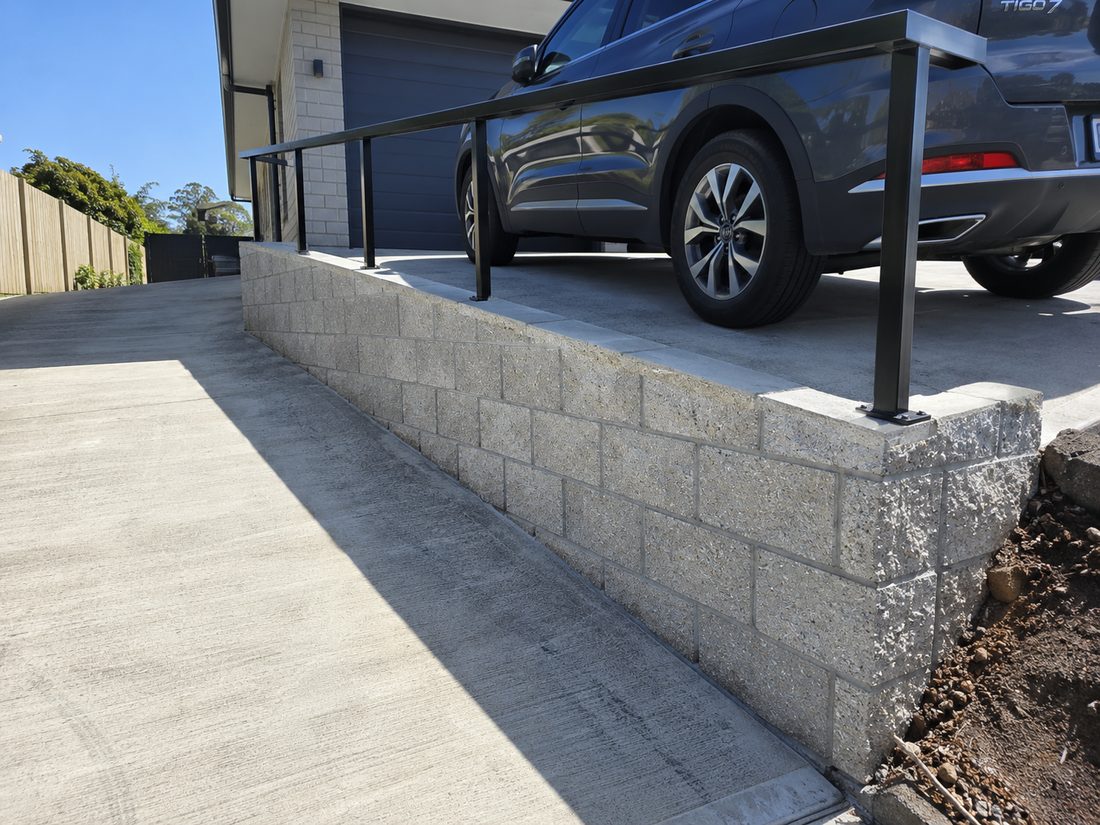 Finished concrete block driveway retaining wall with a black powder coated handrail along the top