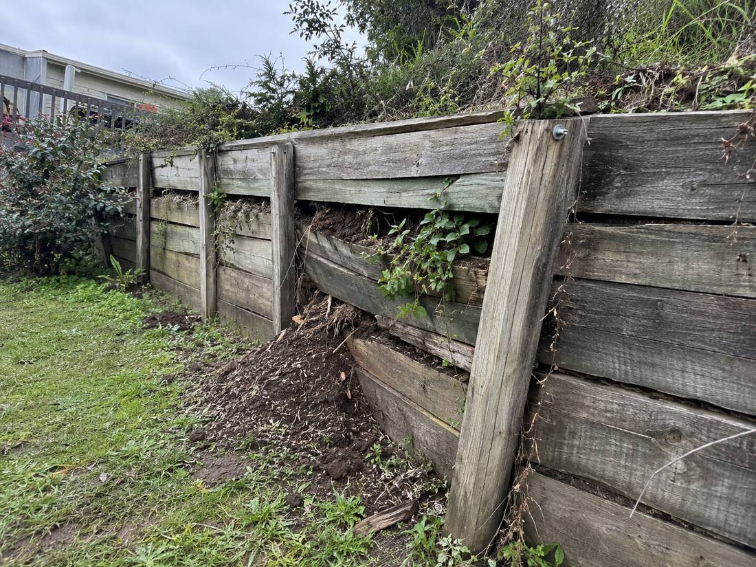 Old timber retaining wall bulging outward with soil spilling through a gap between the sleepers
