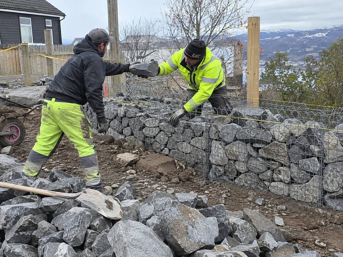 Two workers hand packing angular rock into a galvanised wire gabion basket